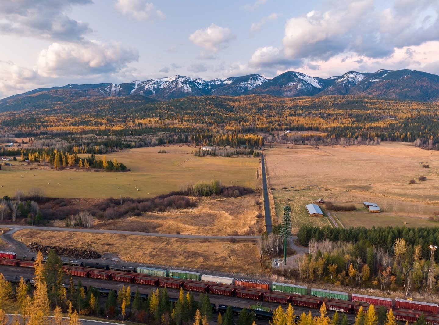 The Flathead Valley at golden hour, with open pastures and a freight train below snow-dusted mountains.